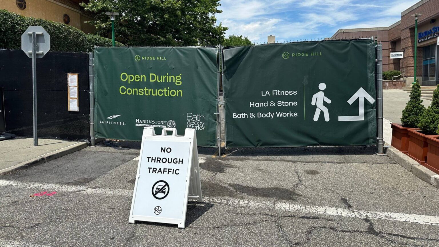 A construction site is blocked off with green tarps labeled "Open During Construction" and "LA Fitness, Hand & Stone, Bath & Body Works" at Ridge Hill